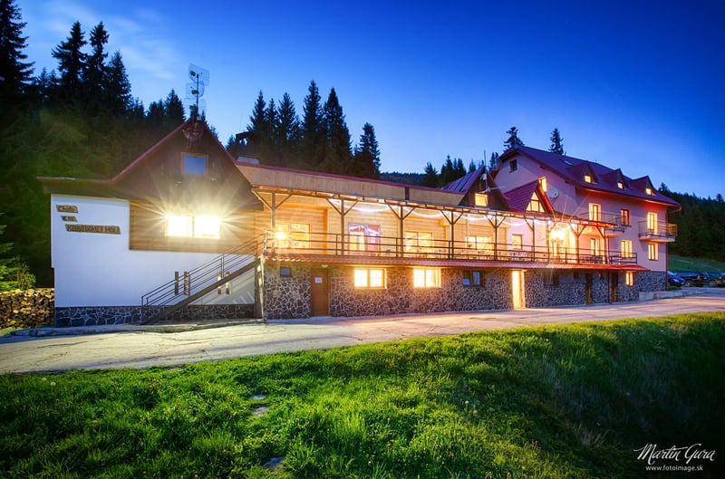 Horský hotel s drevenou fasádou nasvietený podvečer s panorámou hôr v pozadí.