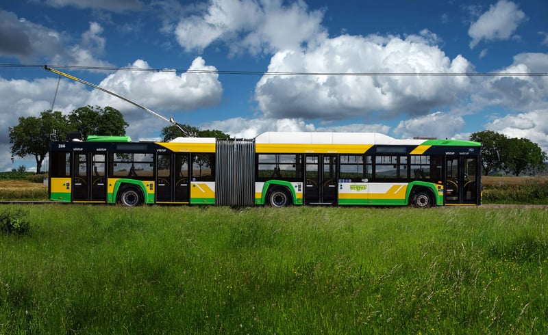 Žltozelený trolejbus Solaris MHD Žilina na vidieckej ceste so stromoradím.
