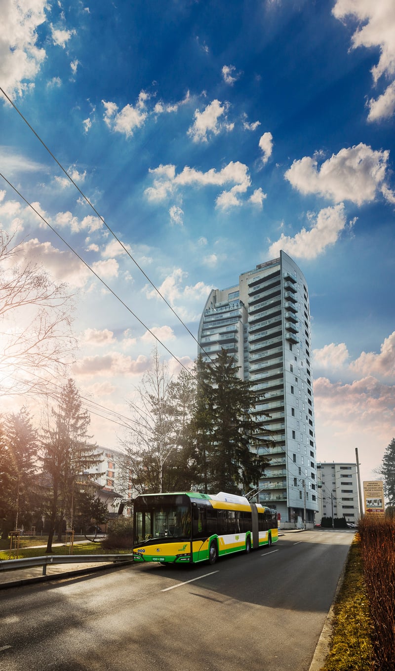 Žltozelený trolejbus Solaris MHD Žilina pred panelovou výškovou bytovkou.