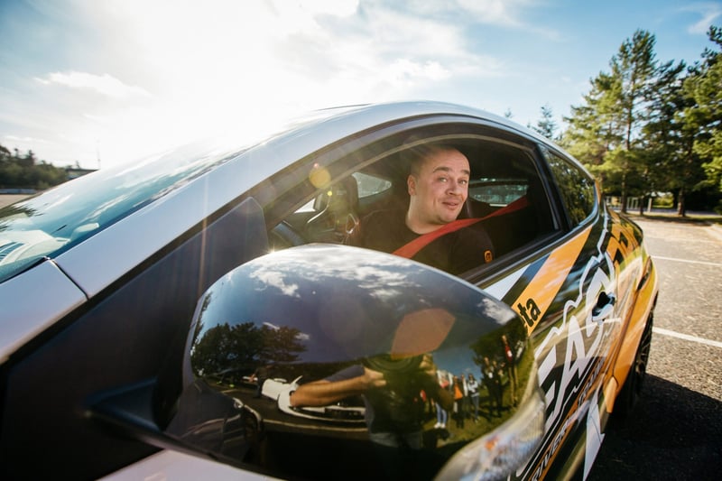 Vodič s úsmevom za volantom driftovacieho auta s polepom počas driving eventu