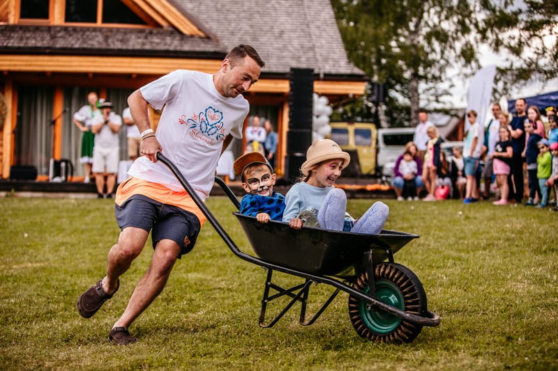 Otec tlačí dvoch usmievajúcich sa chlapcov v záhradnom fúriku počas zábavných pretekov family day-u