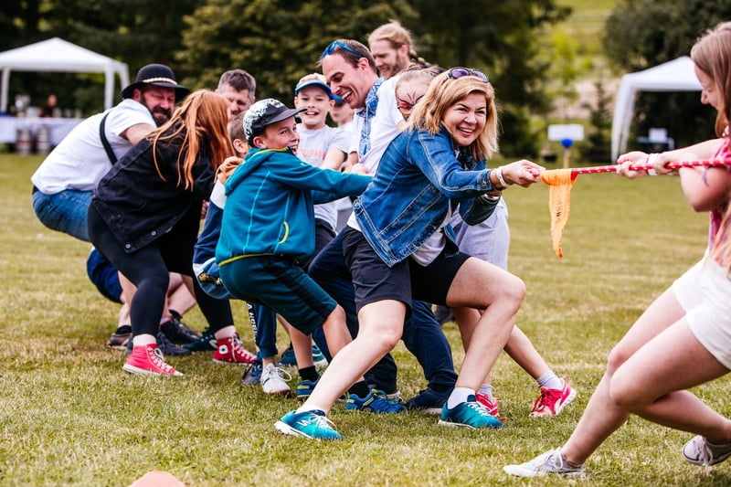 Skupina zamestnancov a ich detí ťahá lano v preťahovaní počas teambuildingu na lúke