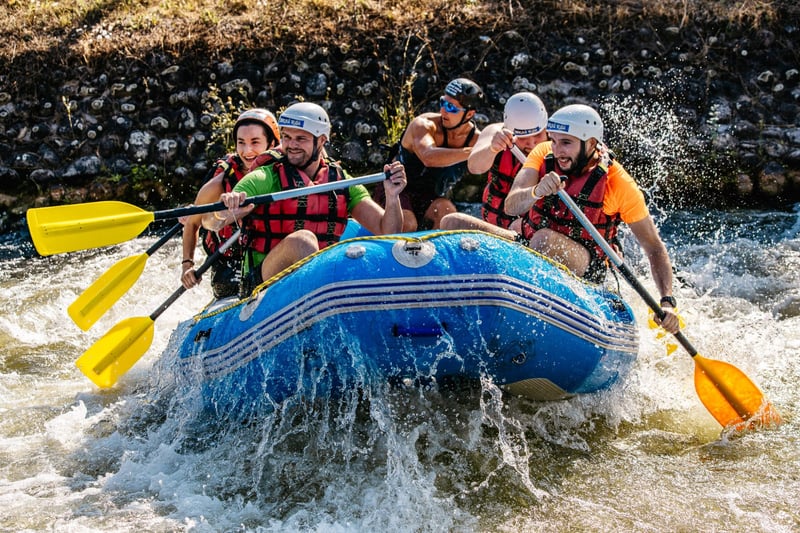 Skupina účastníkov v helmách a vestách pádluje raft cez prudké vlny počas rafting teambuildingu v Čunove