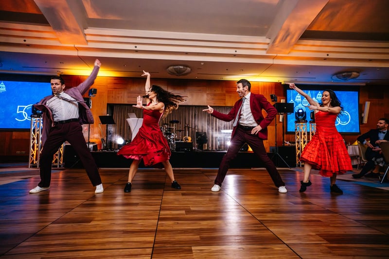 Štyria tanečníci v červených kostýmoch tancujú latino choreografiu na parkete pred kapelou počas firemného večera