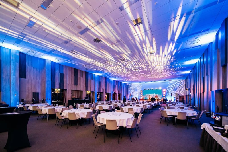 Veľká banketová sála s modrým uplighting osvetlením a pódiom s LED panelom pred firemným večierkom