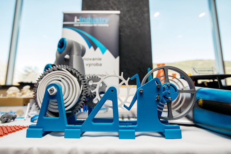 Detail 3D-tlačeného mechanického exponátu s ozubenými kolesami na vystavovateľskom stojane priemyselného veľtrhu