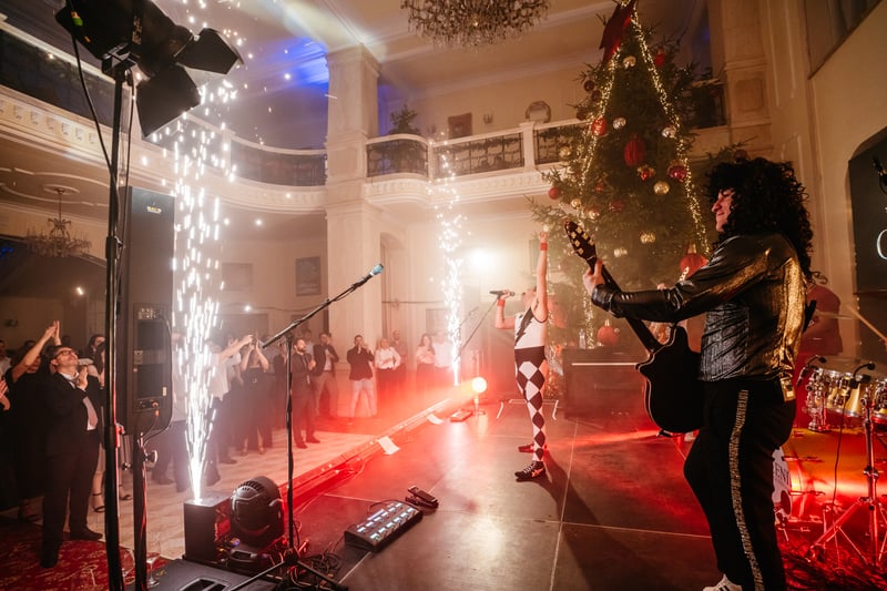 Tribute kapela s gitaristom v paruke pred iskrickovou fontánou a vianočným stromčekom počas firemného vianočného večierka