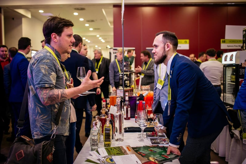 Dvaja účastníci v networkingovej diskusii pri stojane s farebnými drinkmi na gastro veľtrhu