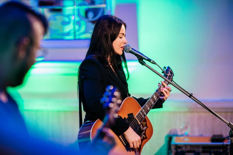 Speváčka s akustickou gitarou pri mikrofóne v zelenom osvetlení pódia