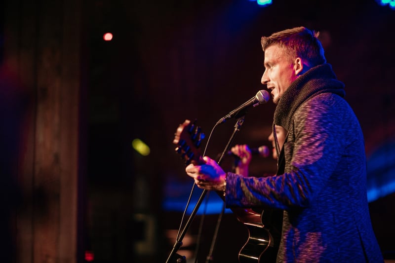 Spevák s gitarou pri mikrofóne v modrom osvetlení pódia