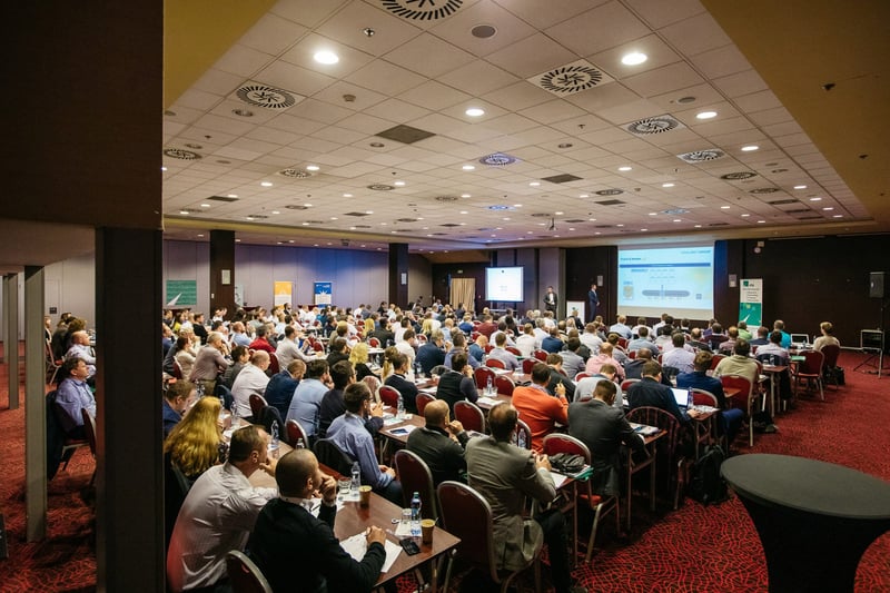 Plná kongresová sála s publikom pri okrúhlych stoloch sleduje keynote prezentáciu