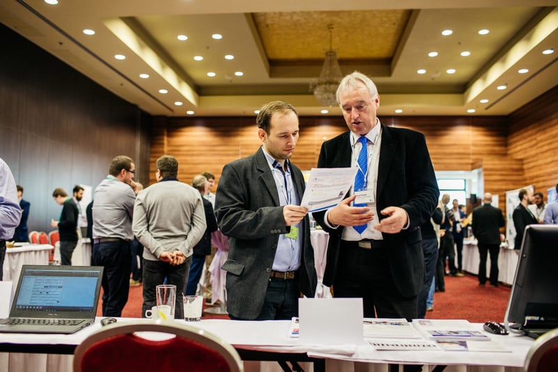 Dvaja účastníci v networkingovej diskusii nad dokumentom pri stoji počas prestávky konferencie