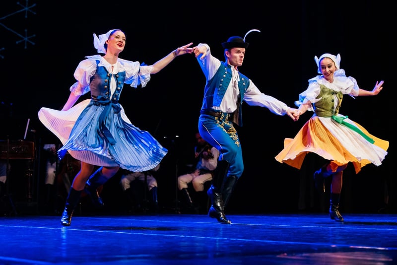 Trojica folklórnych tanečníkov v slovenských krojoch v dynamickom skoku na divadelnom pódiu